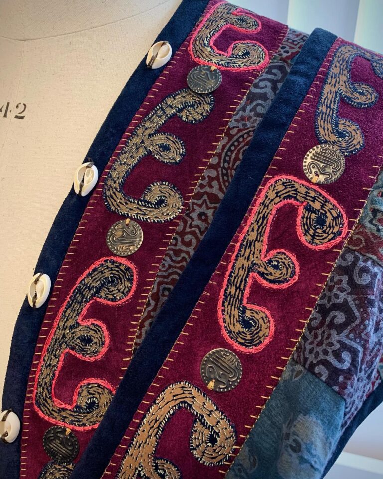 A beaded band of gold paisley embroidery on indigo and crimson silk, finished with cowrie shells and coins