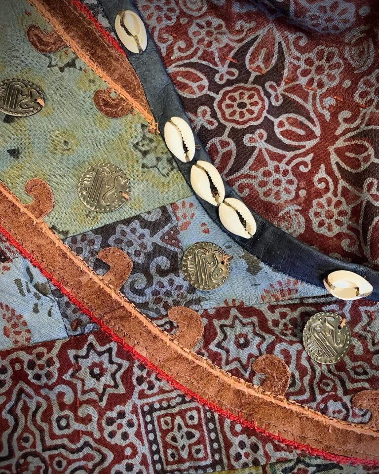 An embroidered tabard border in gold and red thread, edged with hand-stitched cowrie shells and coins