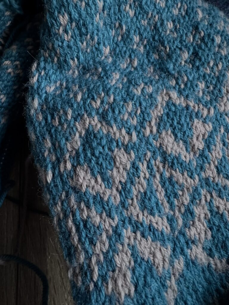 Close-up of hand-knitted colourwork in teal and pale grey wool