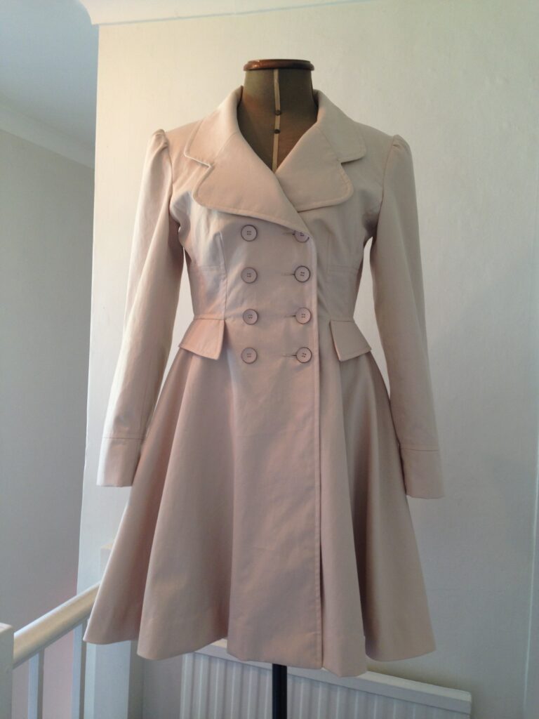 A pale pink double-breasted coat with a flared skirt on a dress stand